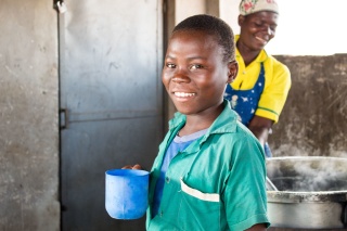child smiling and looking at the camera with blue mug of porridge in his hand