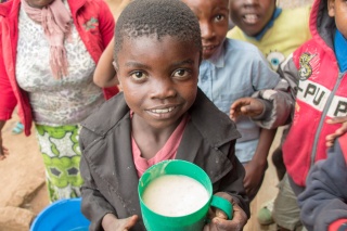 young girl looking up at camera with a mug of porridge in her hands