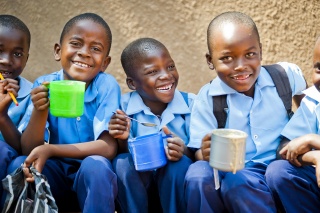 Group of children smiling holding mugs of food in their hands.
