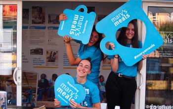 A group of Mary's Meals volunteers smiling and holding Mary's Meals mugs