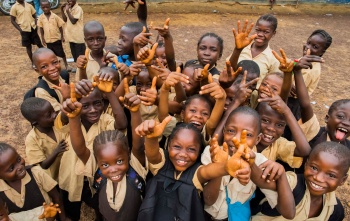 A group of children smiling and waving as they attend school in Liberia.
