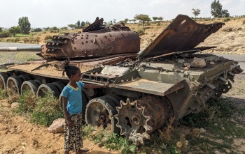 Image of a child standing next to an abandoned tank by the roadside.