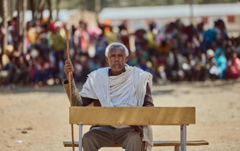 A village elder sits at a desk against the backdrop of a crowd which had gathered.