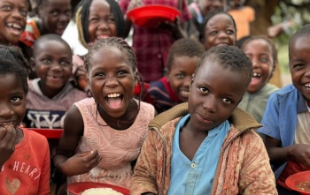 A group of school children posing with plates of food and looking into camera.