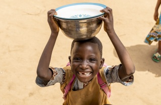 small boy smiling at the camera whilst balancing a large metallic bowl on his head