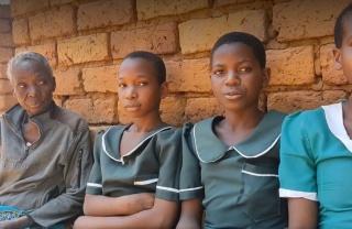 four women sitting against a wall, one is older than the other three