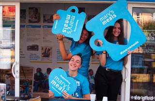 A group of Mary's Meals volunteers smiling and holding Mary's Meals mugs