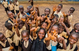 A group of children smiling and waving as they attend school in Liberia.