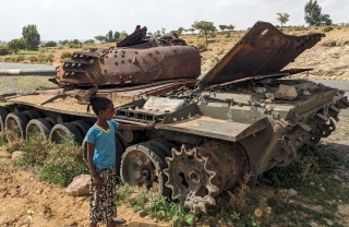 Image of a child standing next to an abandoned tank by the roadside.