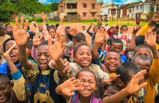 Children outside school smiling, waving and looking into camera.
