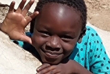 Photo of a single child leaning on a wall, smiling and looking up to the camera.