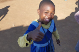 Image of a child smiling and giving a thumbs up gesture to the camera.