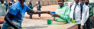 a queue of people collecting food from a woman serving behind a table