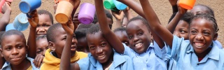 a group of children holding bright coloured mugs aloft