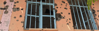 Image of windows with bullet holes strewn on the surrounding walls. 