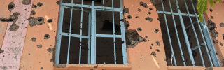 Image of windows with bullet holes strewn on the surrounding walls.