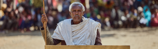 Village elder in Tigray sitting at a desk against the backdrop of a crowd which had gathered.