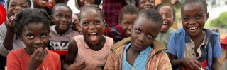 A group of school children posing with plates of food and looking into camera.