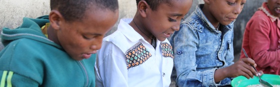 children sitting in a line eating from plates of food