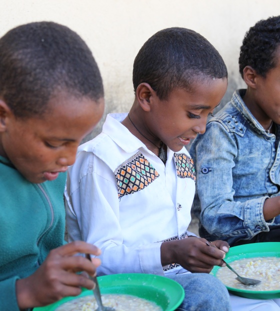 children sitting in a line eating from plates of food
