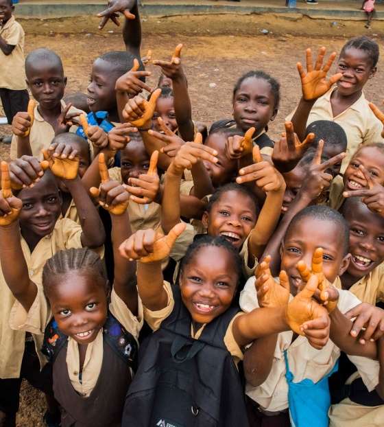 A group of children smiling and waving as they attend school in Liberia.