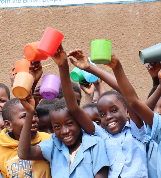 a group of children holding bright coloured mugs aloft
