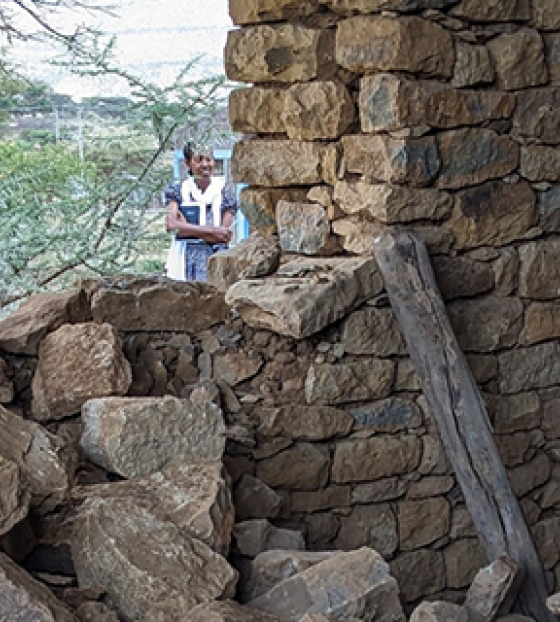Mary's Meals volunteer standing in a building where one of the walls has collapsed.