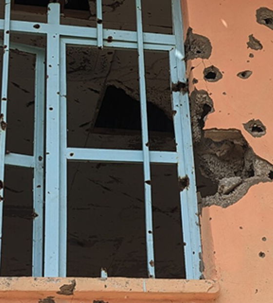 Image of windows with bullet holes strewn on the surrounding walls. 