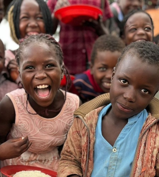 A group of school children posing with plates of food and looking into camera.