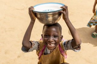 small boy smiling at the camera whilst balancing a large metallic bowl on his head