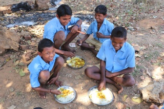 young boys kneeling on the ground eating from silver plates of food