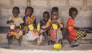 young children sitting against a wall smiling to the camera