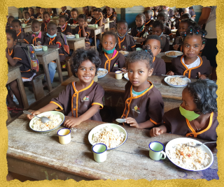 children in class sitting on the floor with plates of food in front