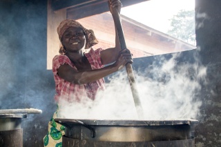 Woman stirring a large, steaming cauldron of hot food