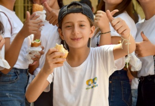 A boy gives a thumbs up to camera as he eats in Syria