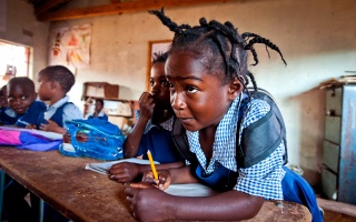A girl leans forward eagerly as she writes during a lesson