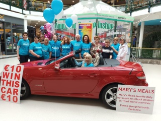 group of Mary's Meals volunteers posing for a photo in front of a prize car