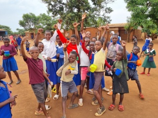 A group of children smiling and waving to the camera.