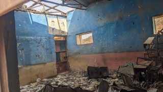 Image showing a classroom with debris scattered across the room as a result of recent conflict.