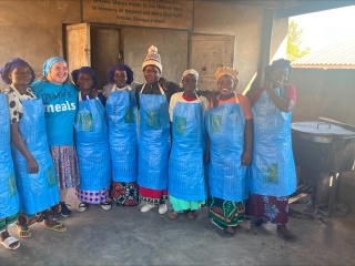 A group of Mary's Meals volunteer cooks posing for a photo in the school kitchen with a board member of Mary's Meals Ireland. 