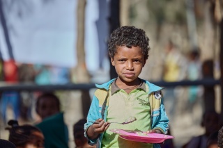 Image of a child holding a plate of food and looking into camera.