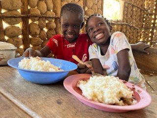 Image of two children smiling at a table with two plates of food in front of them. 