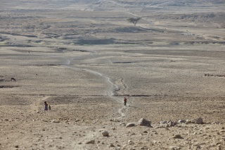 Figures seen walking in the distance against a vast desert landscape.